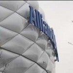 Eine Nahaufnahme der Außenseite eines Gebäudes mit dem „Allianz Arena“-Logo auf der Fassade, mit einem Teil eines kahlen Astes im Vordergrund. Fritten, Fussball & Bier - www.soccer-warriors.de