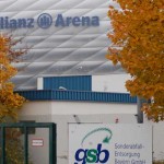 Außenansicht der Allianz Arena mit Herbstlaub auf einem normalen Bundesligasamstag und einem daneben liegenden Firmenschild. Fritten, Fussball & Bier - www.soccer-warriors.de