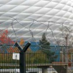 Eine moderne Kuppel der Allianz Arena hinter einem Sicherheitszaun mit Stacheldraht. Fritten, Fussball & Bier - www.soccer-warriors.de