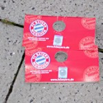 Ein weggeworfener Flyer des FC Bayern München auf einer Kopfsteinpflasterfläche anlässlich des Bundesligasamstags. Fritten, Fussball & Bier - www.soccer-warriors.de