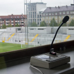 Ein Mikrofon und ein Bedienfeld in einer Sportkommentatorenbox mit Blick auf den Fußballplatz im Grünwalder Stadion. Fritten, Fussball & Bier - www.soccer-warriors.de