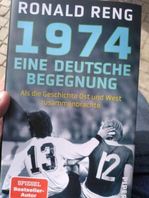 Cover des Buches „1974 – Eine deutsche Begegnung“ von Ronald Reng, mit zwei Fußballspielern und verschwommenen Fans im Hintergrund. Fritten, Fussball & Bier - www.soccer-warriors.de